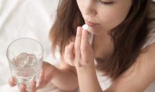 Girl taking white pill and holding glass of water