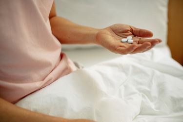 woman sitting on bed holding three white round pills