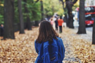 Little girl wearing blue backpack on a sidewalk in an urban area