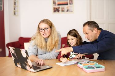 Mom and dad sitting at table with daughter helping with homework