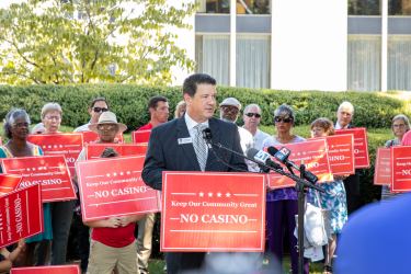 John Rustin speaking at a press conference surrounded by people holding "No Casino" signs