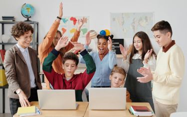 Children at school sitting around two laptops celebrating an opportunity