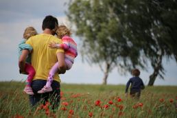 Father walking through field with three children