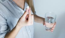 Woman taking a white pill with a glass of water