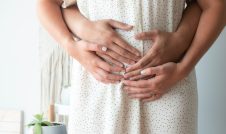 Husband hugging wife with their hands on her pregnant belly