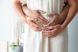 Husband hugging wife with their hands on her pregnant belly